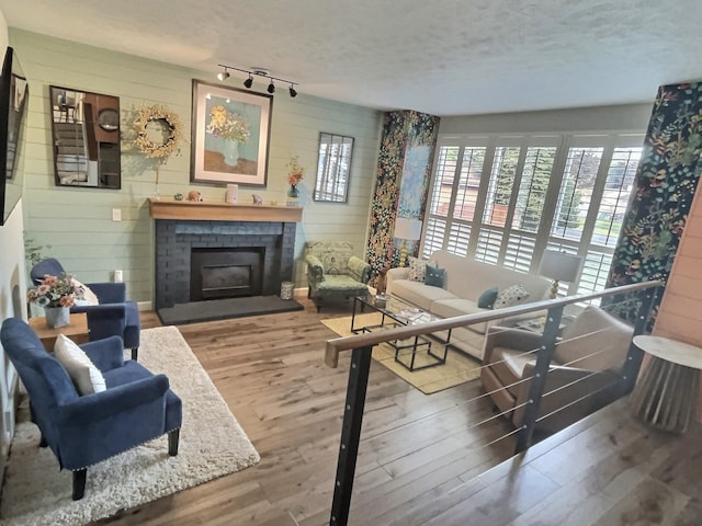 living area featuring a textured ceiling, wood walls, a brick fireplace, and wood finished floors