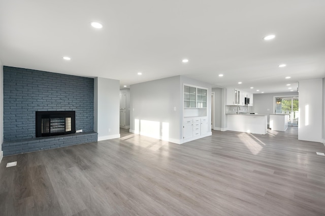 unfurnished living room featuring baseboards, light wood-type flooring, a brick fireplace, and recessed lighting