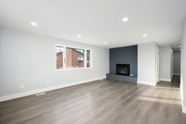 unfurnished living room with baseboards, visible vents, wood finished floors, a fireplace, and recessed lighting