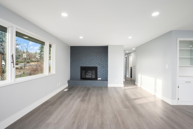 unfurnished living room featuring recessed lighting, a brick fireplace, baseboards, and light wood finished floors