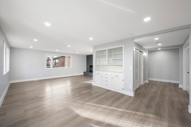 unfurnished living room featuring recessed lighting, a fireplace, baseboards, and wood finished floors