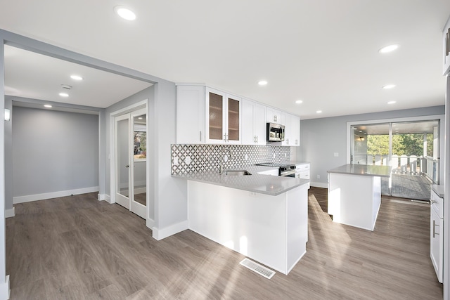 kitchen with a sink, visible vents, appliances with stainless steel finishes, decorative backsplash, and glass insert cabinets