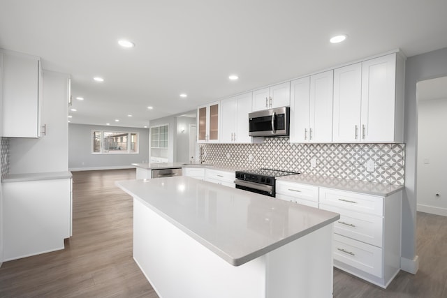 kitchen with tasteful backsplash, light countertops, appliances with stainless steel finishes, white cabinetry, and wood finished floors