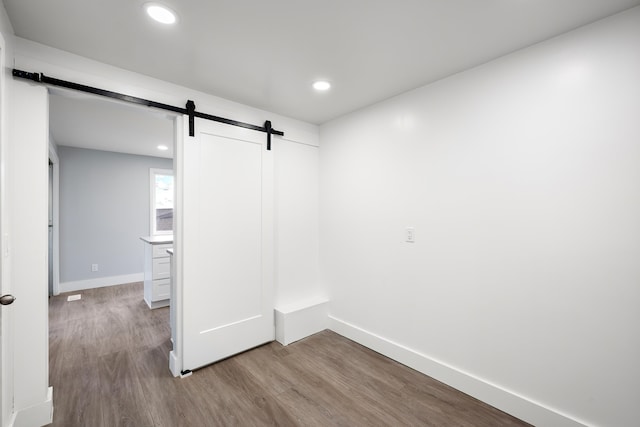 spare room with a barn door, recessed lighting, wood finished floors, and baseboards