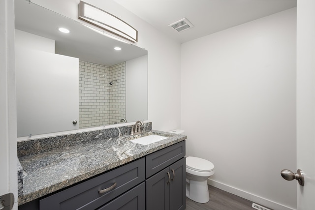 full bathroom with baseboards, visible vents, toilet, a tile shower, and vanity