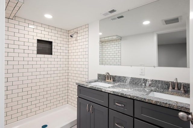 full bathroom featuring a tile shower, a sink, and visible vents