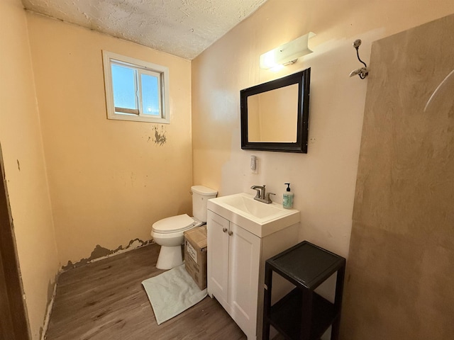 half bath featuring toilet, a textured ceiling, wood finished floors, and vanity