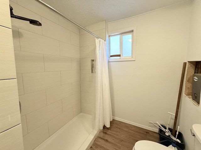 bathroom featuring baseboards, toilet, wood finished floors, a tile shower, and a textured ceiling