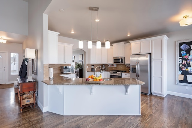 kitchen featuring appliances with stainless steel finishes, stone counters, a peninsula, and a kitchen bar