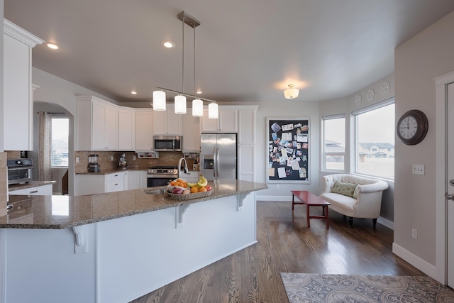 kitchen with arched walkways, stainless steel appliances, a breakfast bar area, and white cabinets