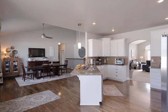 kitchen with light stone counters, arched walkways, white cabinets, vaulted ceiling, and a peninsula