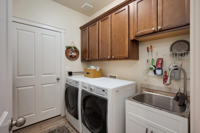 washroom featuring cabinet space, visible vents, independent washer and dryer, light wood-style floors, and a sink