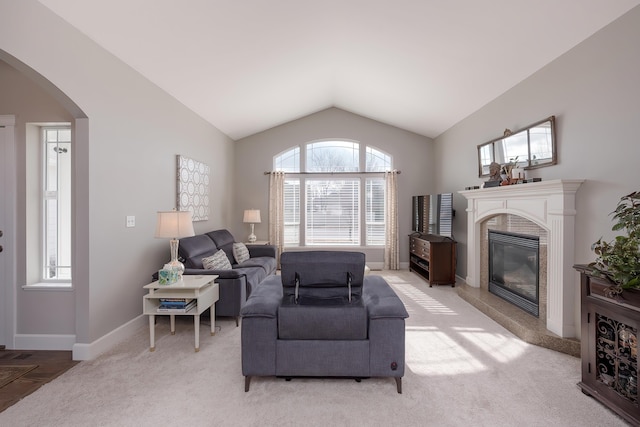 living area with baseboards, arched walkways, light colored carpet, vaulted ceiling, and a fireplace