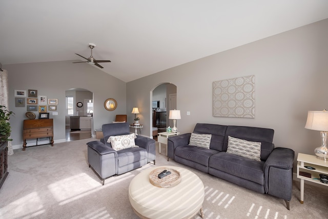 living room with arched walkways, light colored carpet, a ceiling fan, baseboards, and vaulted ceiling