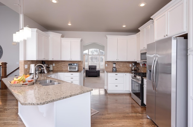 kitchen with light stone counters, a peninsula, a sink, white cabinetry, and appliances with stainless steel finishes