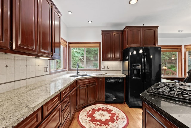 kitchen featuring decorative backsplash, a sink, light stone countertops, light wood-type flooring, and black appliances