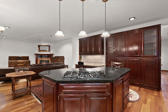 kitchen featuring light wood-style floors, a glass covered fireplace, stainless steel gas stovetop, and backsplash