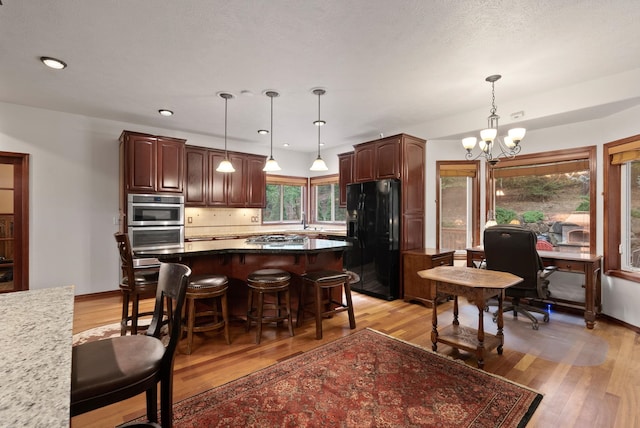 kitchen featuring light wood-style flooring, a kitchen breakfast bar, stainless steel appliances, a chandelier, and backsplash