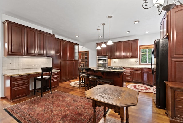 kitchen with a breakfast bar area, stainless steel appliances, wood finished floors, a kitchen island, and built in study area