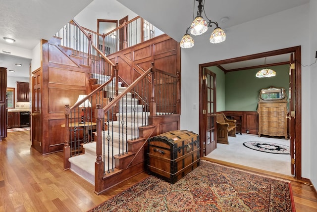 stairway with a towering ceiling, an inviting chandelier, and wood finished floors