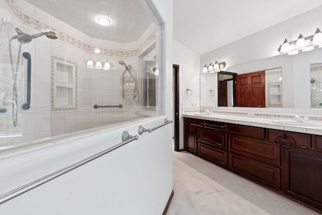 bathroom featuring a tile shower, double vanity, a sink, and lofted ceiling