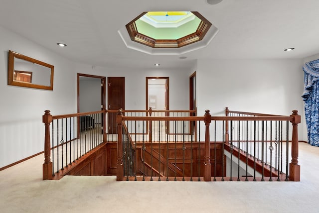 hall featuring carpet floors, a raised ceiling, and an upstairs landing