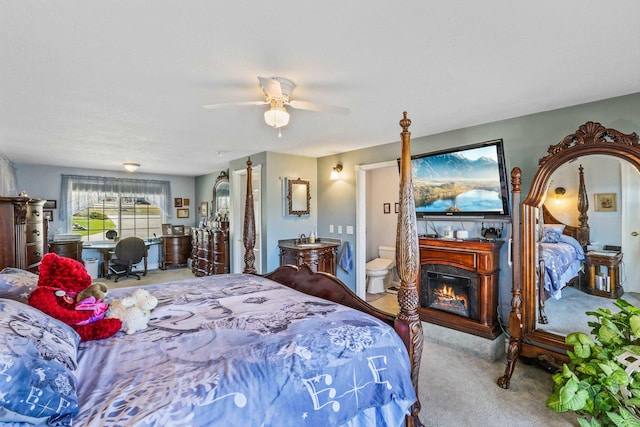 carpeted bedroom with a glass covered fireplace, ceiling fan, and ensuite bath