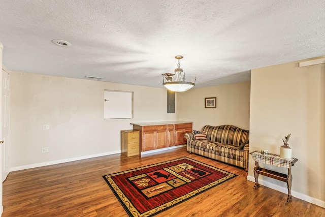 living area featuring a textured ceiling, wood finished floors, visible vents, and baseboards