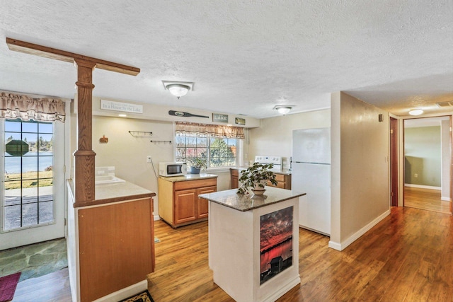 kitchen with decorative columns, light countertops, a textured ceiling, wood finished floors, and white appliances