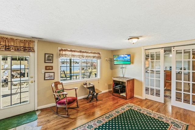 living area with visible vents, baseboards, wood finished floors, a textured ceiling, and french doors