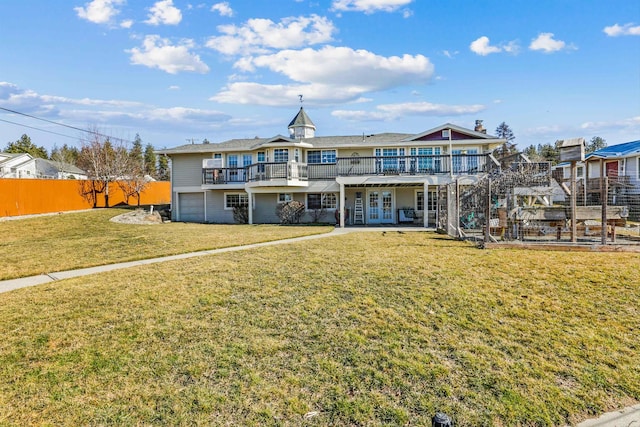 rear view of house with driveway, a lawn, an attached garage, fence, and french doors