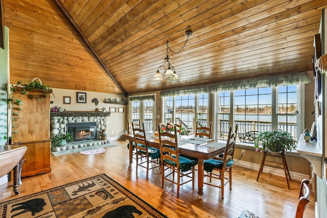 dining area with a water view, vaulted ceiling, hardwood / wood-style floors, and a stone fireplace