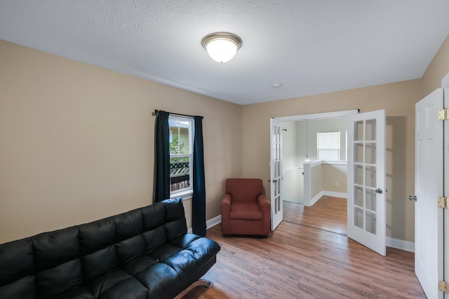 living room with french doors, a textured ceiling, baseboards, and wood finished floors