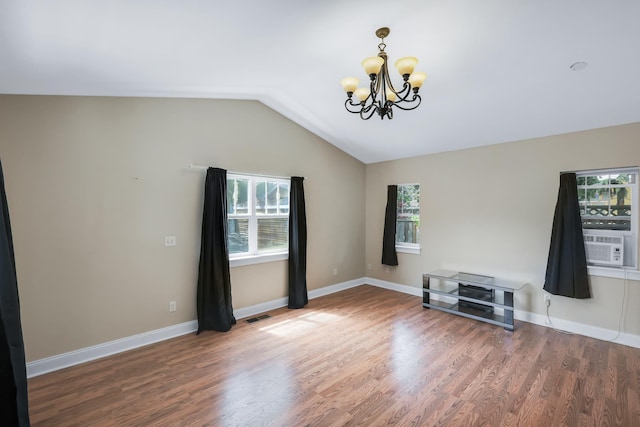 empty room featuring lofted ceiling, a chandelier, wood finished floors, visible vents, and baseboards