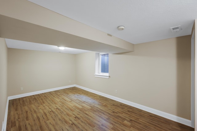 below grade area featuring wood finished floors, visible vents, and baseboards