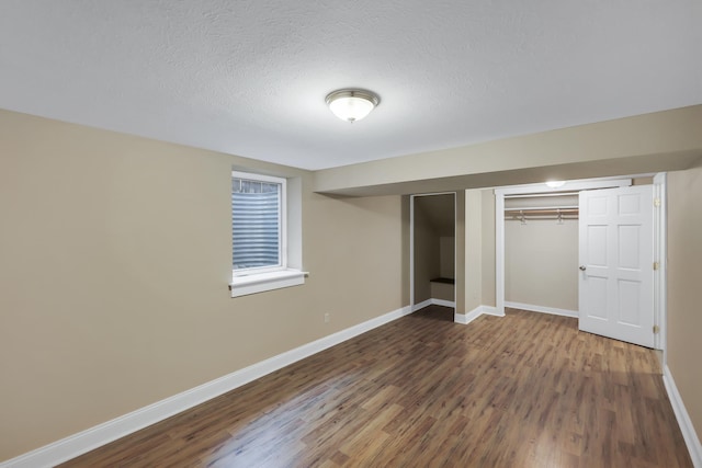 unfurnished bedroom with a textured ceiling, baseboards, and wood finished floors