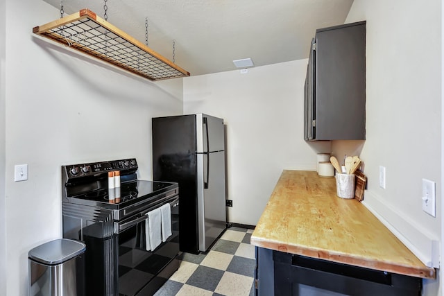 kitchen featuring light floors, light countertops, black electric range oven, freestanding refrigerator, and baseboards