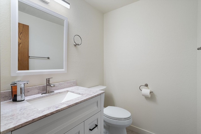 half bath with baseboards, vanity, and toilet