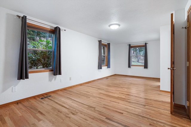 spare room featuring baseboards, a textured ceiling, visible vents, and light wood-style floors