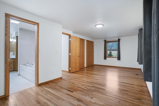 unfurnished bedroom with light wood finished floors, baseboards, multiple closets, and ensuite bathroom