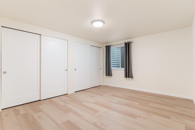 unfurnished bedroom with light wood finished floors, baseboards, and multiple closets