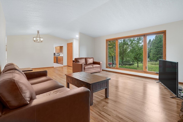 living room featuring light wood-type flooring, lofted ceiling, a notable chandelier, and a textured ceiling