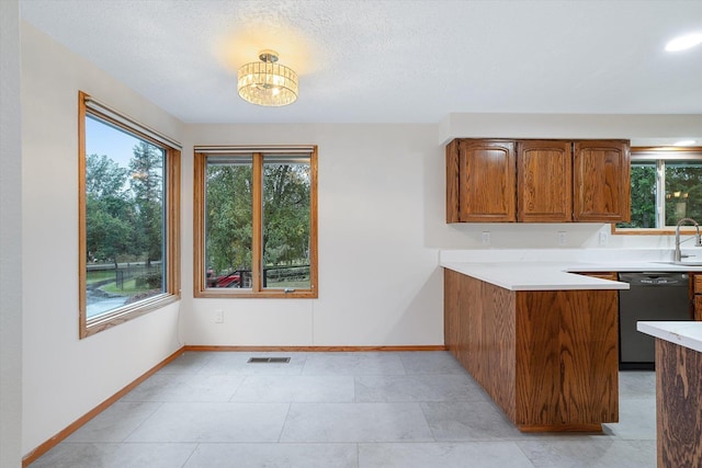 kitchen featuring black dishwasher, visible vents, brown cabinetry, light countertops, and a sink