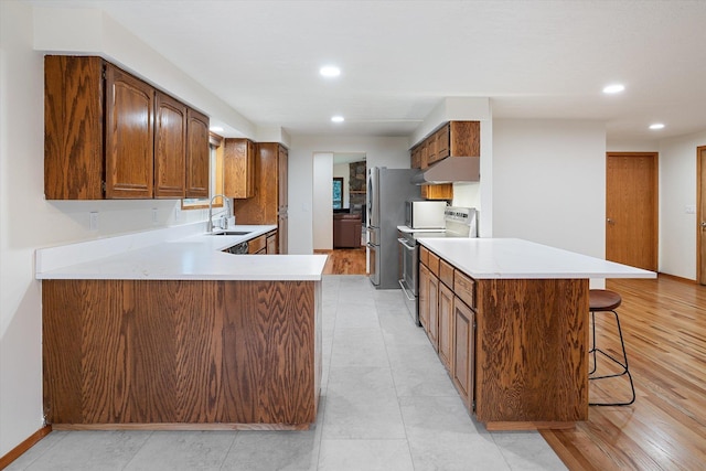 kitchen featuring under cabinet range hood, stainless steel appliances, a peninsula, a sink, and light countertops