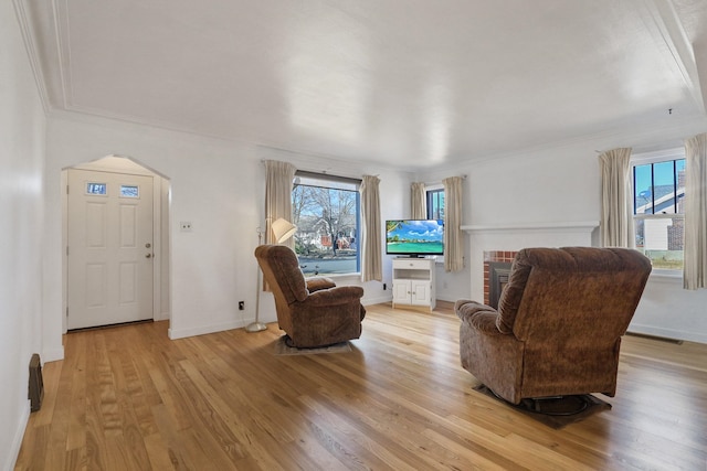 sitting room featuring arched walkways, a brick fireplace, baseboards, and light wood-style floors