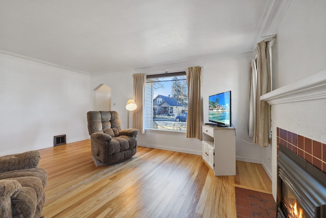 sitting room featuring arched walkways, visible vents, a tiled fireplace, ornamental molding, and wood finished floors