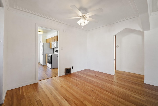 empty room with arched walkways, visible vents, light wood-style floors, ornamental molding, and ceiling fan