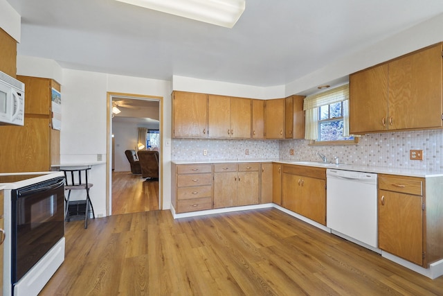 kitchen featuring light wood finished floors, light countertops, white appliances, and backsplash