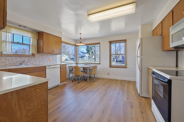 kitchen with white appliances, a sink, light countertops, decorative backsplash, and brown cabinetry