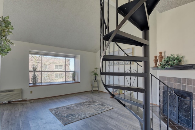 stairway with lofted ceiling, wood finished floors, a wall mounted air conditioner, a textured ceiling, and a fireplace